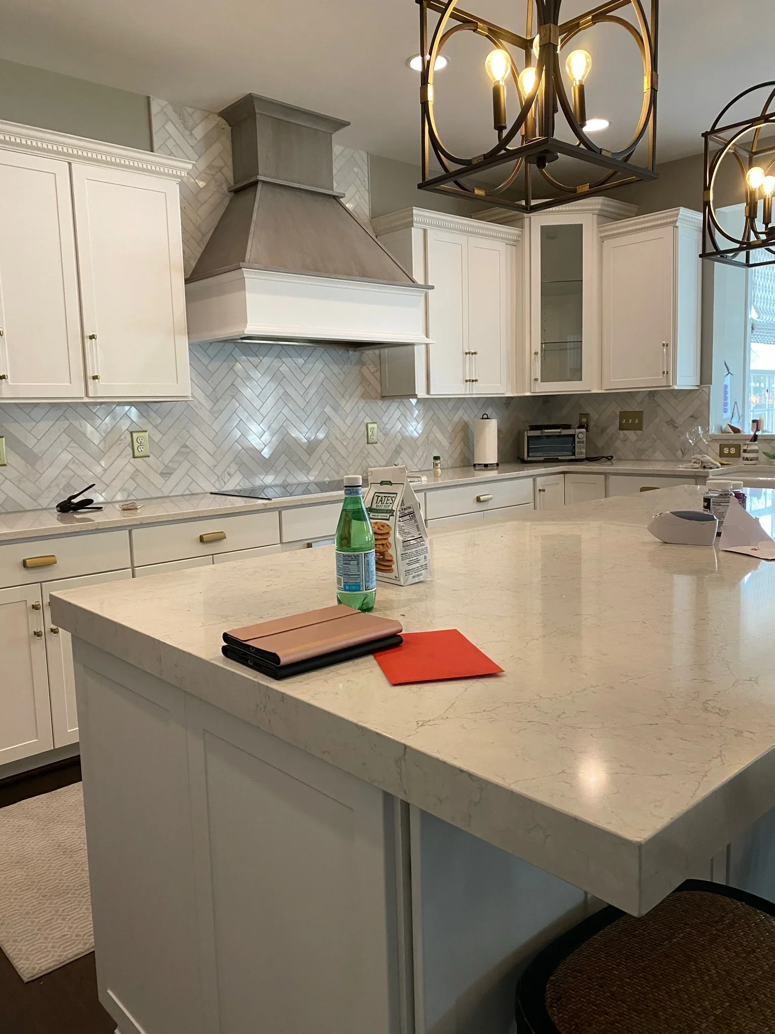 White kitchen with marble island, herringbone backsplash, brass fixtures, and custom range hood