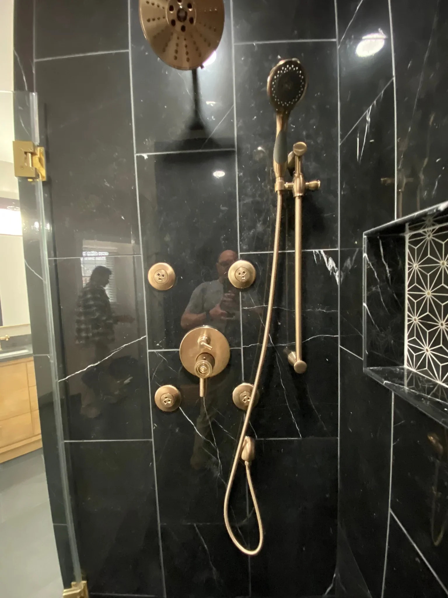 Black marble tile shower with brass fixtures, rainfall showerhead, and body jets