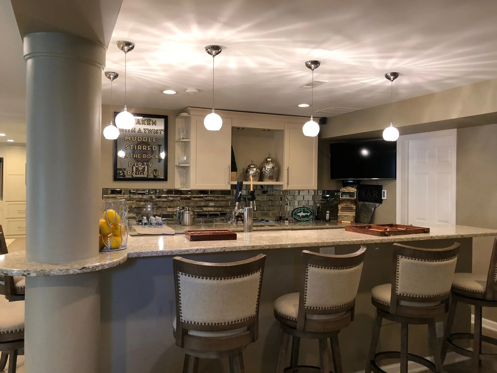 Granite island bar with upholstered seating, subway tile backsplash, pendant lights, and built-in cabinetry