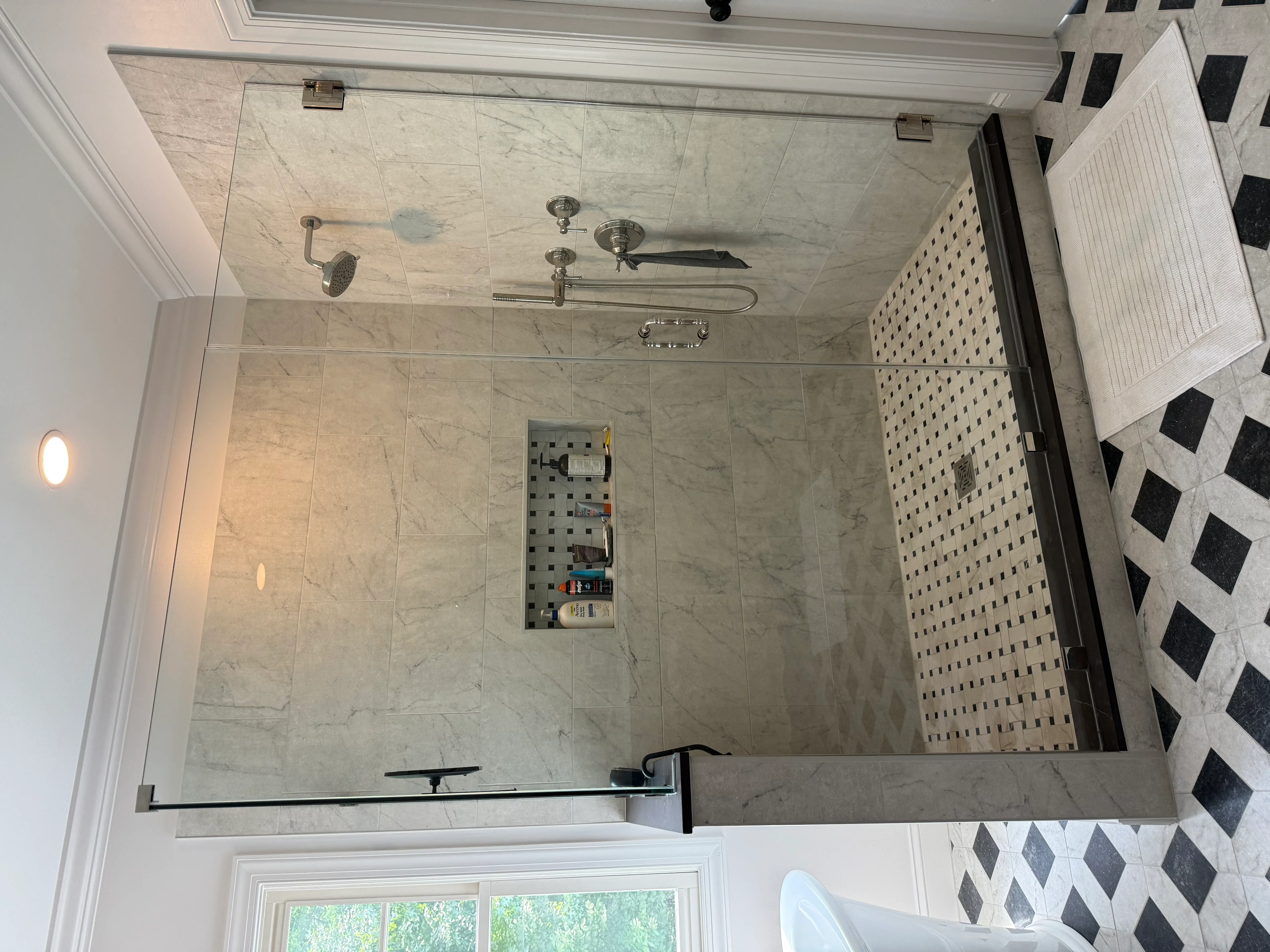 Marble tile shower with rainfall head, body sprays, frameless glass enclosure, and geometric floor tile