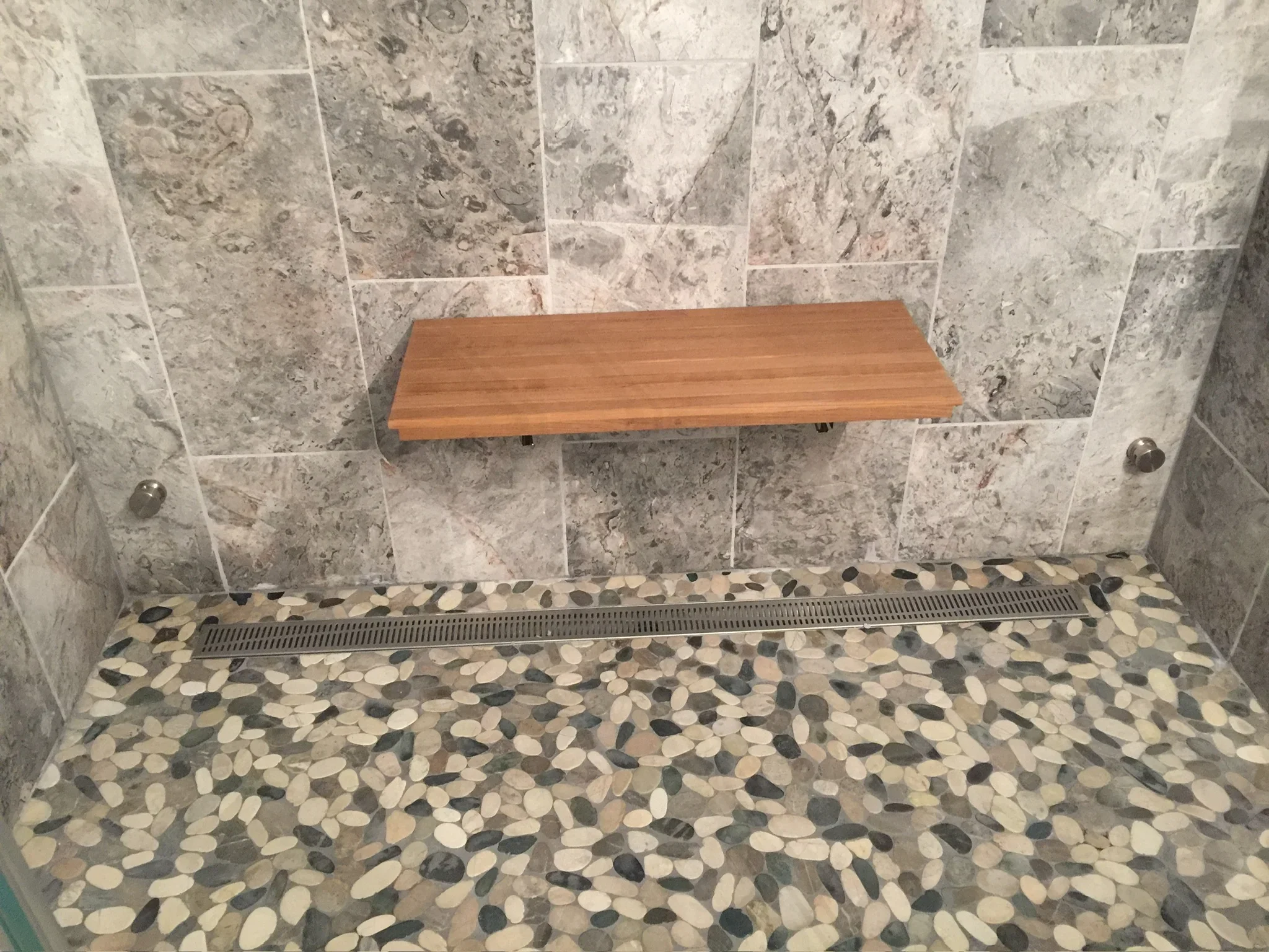 Travertine tile shower walls with pebble mosaic floor and cedar wood bench