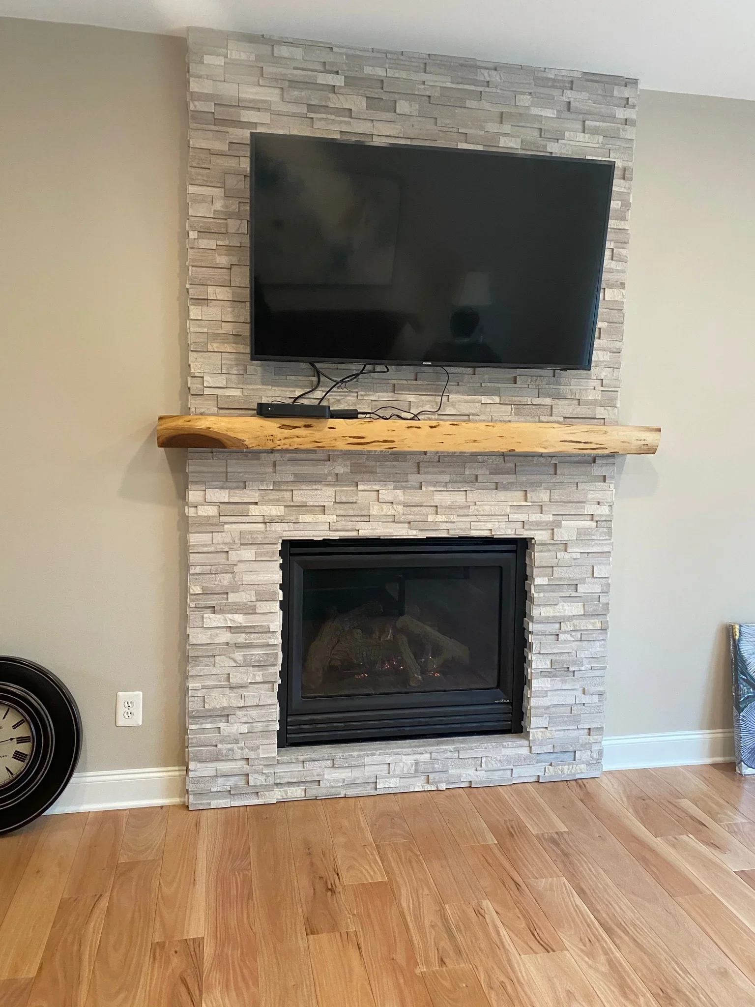 Stacked stone fireplace surround with black insert, floating wood shelf, and mounted TV