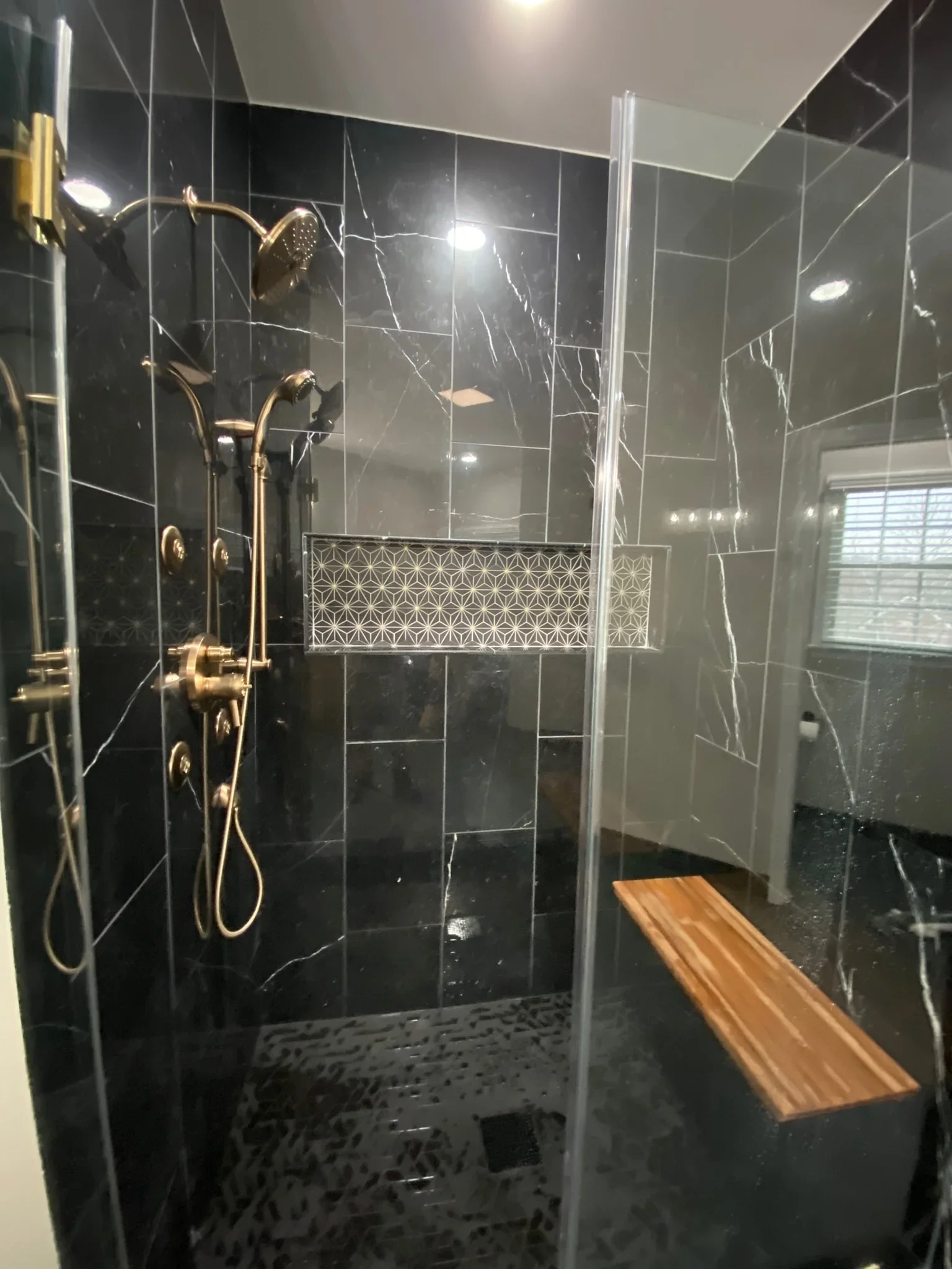 Black marble tile shower with gold fixtures, geometric accent tile, and frameless glass enclosure