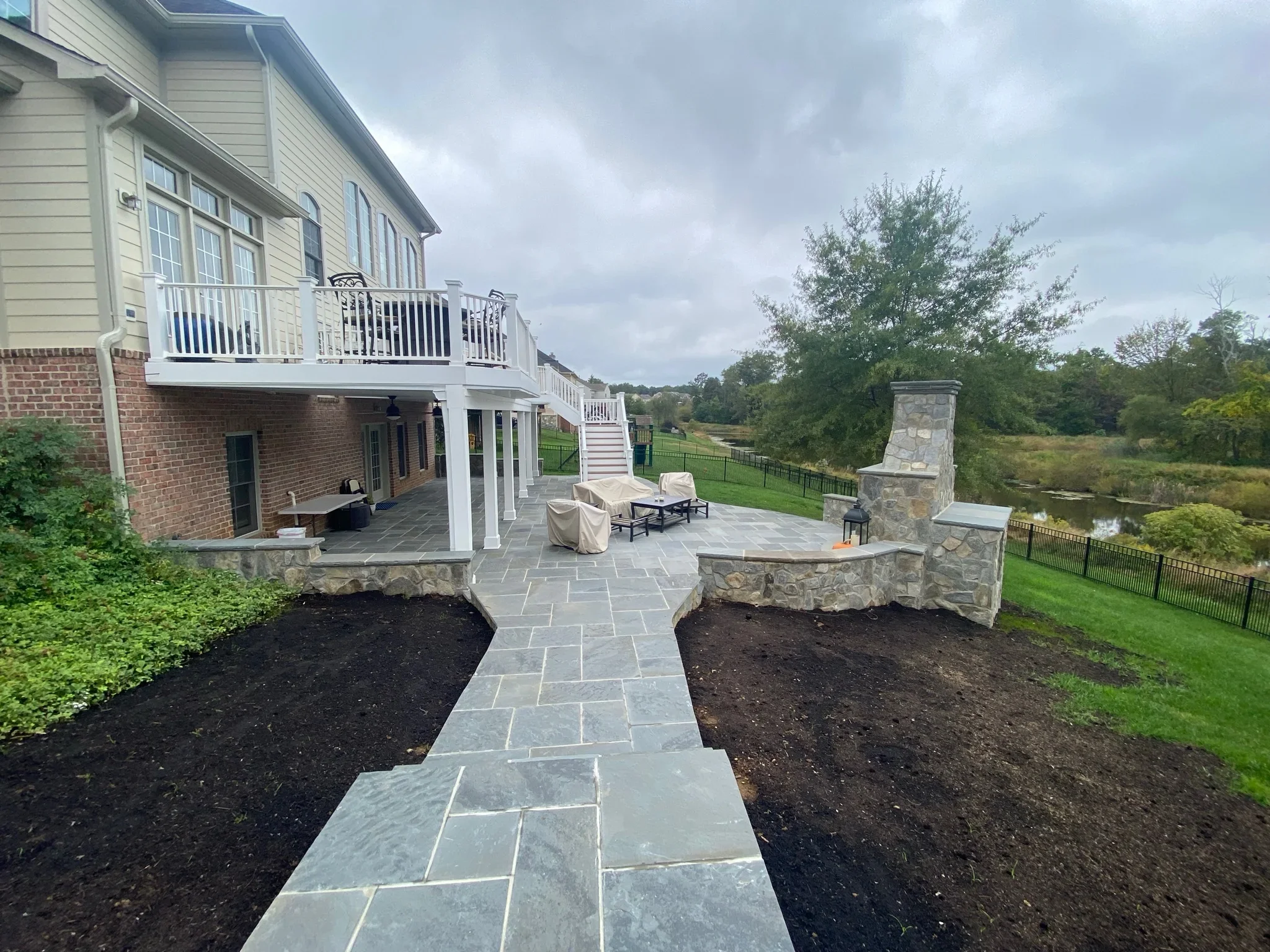 Bluestone patio with stone planters, white deck, and chimney overlooking landscaped grounds