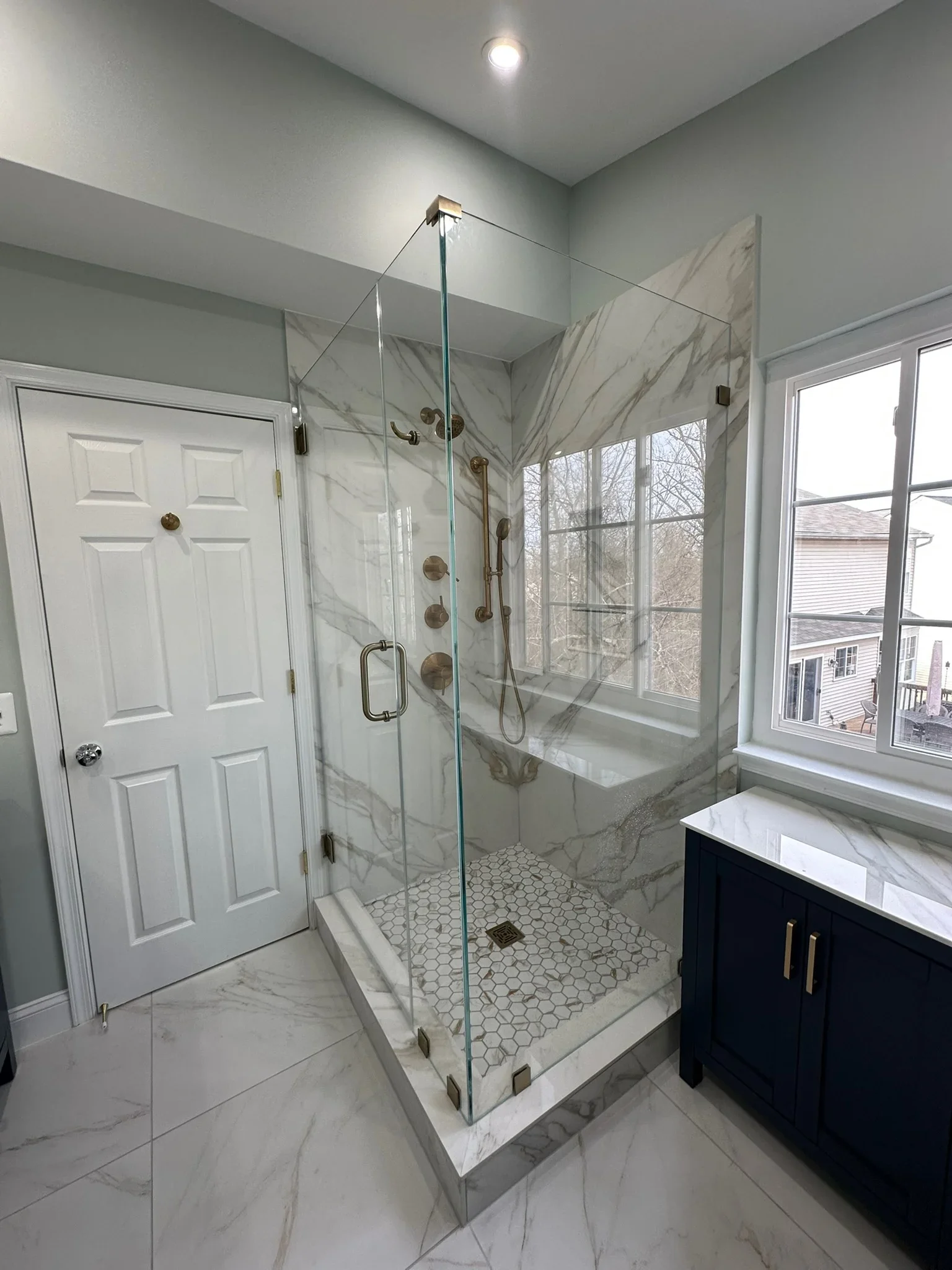 Frameless glass shower with marble tile walls, hexagonal floor tile, and bronze fixtures