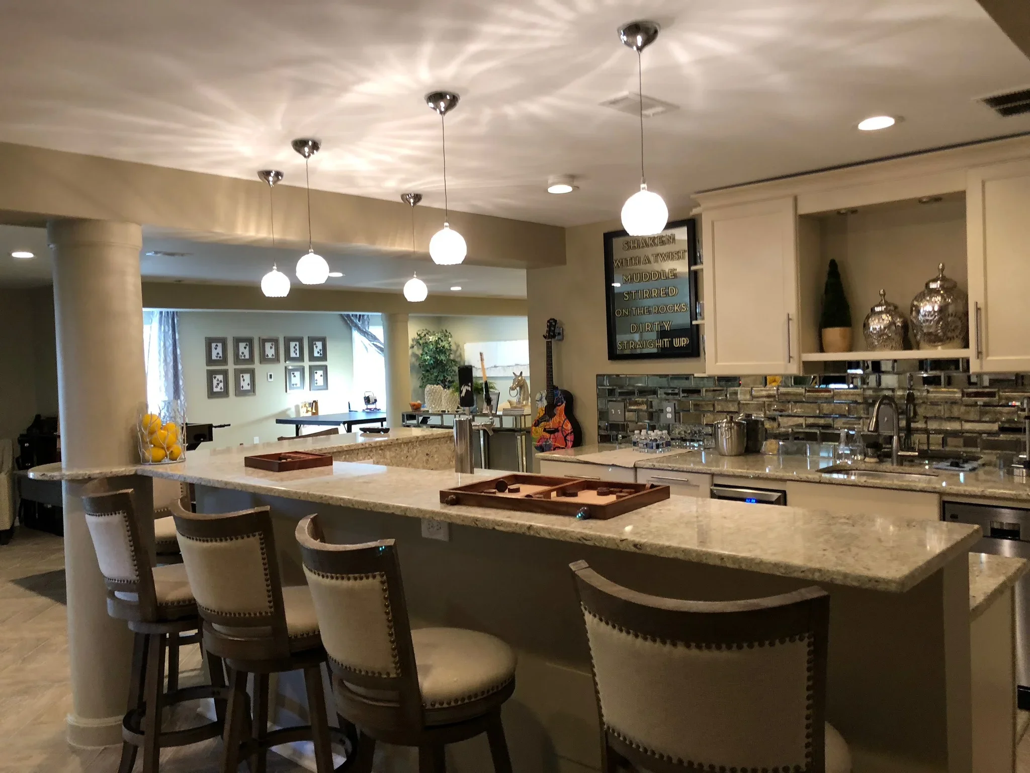 Modern kitchen with granite island, glass tile backsplash, white cabinetry, and pendant lighting