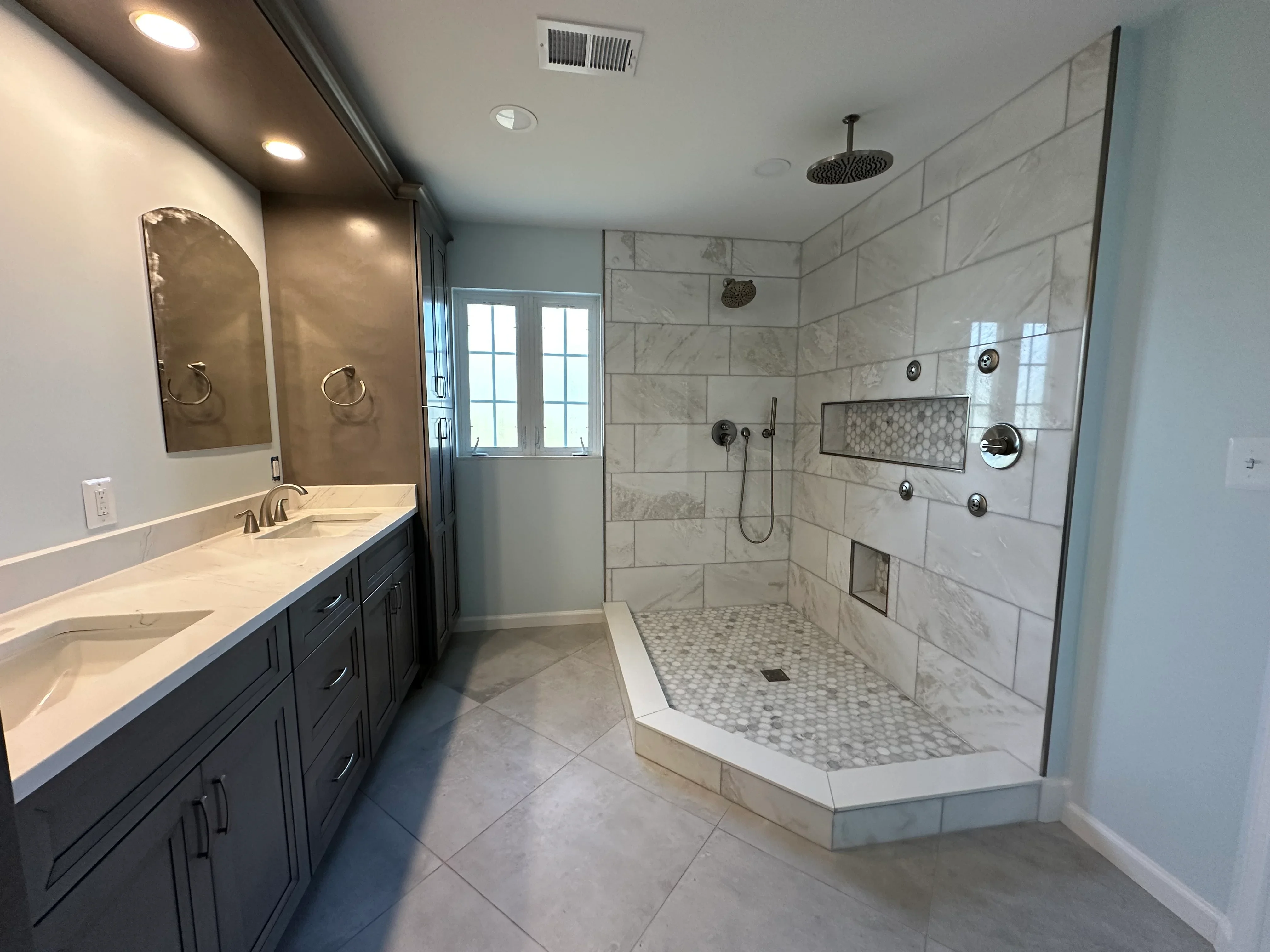Master bathroom with marble tile shower, dark vanity, and hexagonal mosaic floor