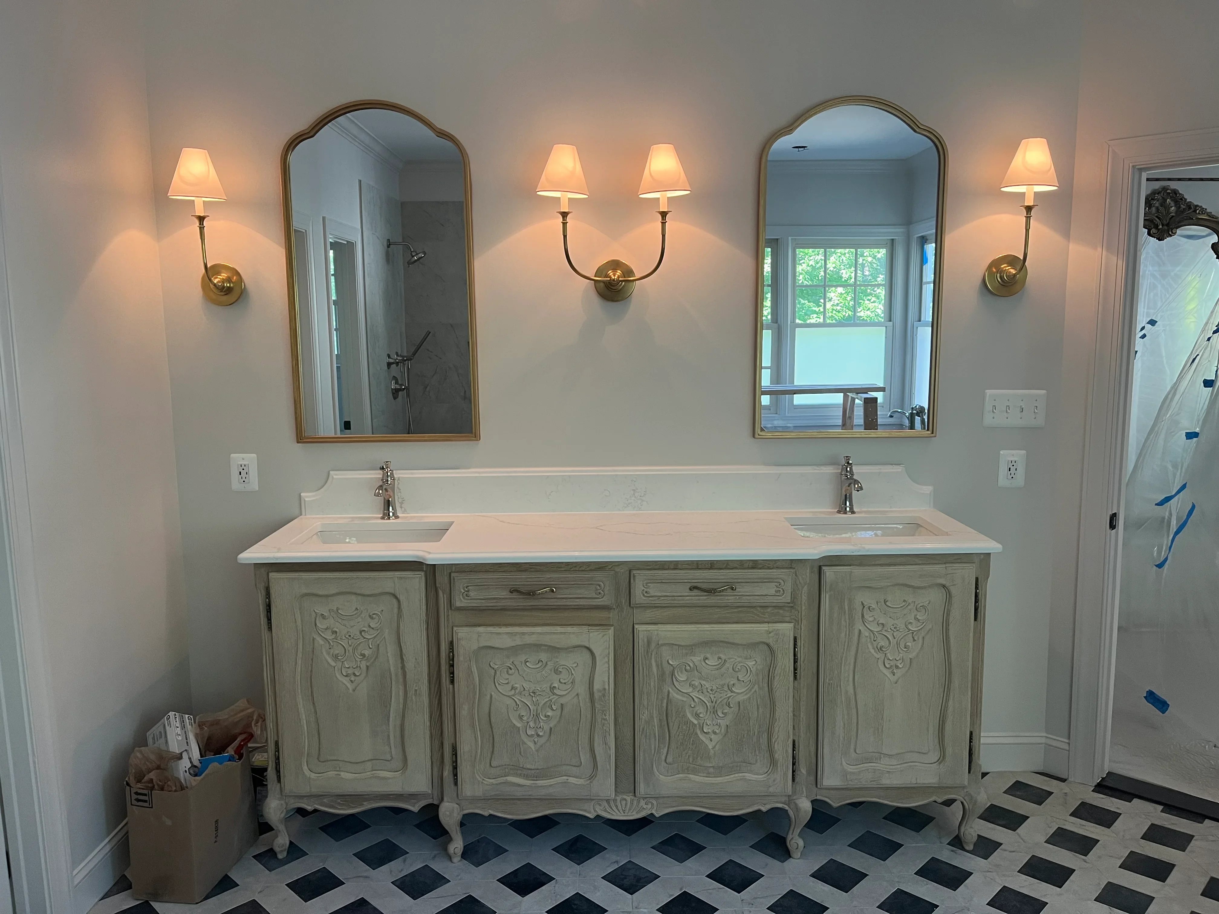 Dual-sink vanity with carved wood cabinet, marble countertop, brass sconces, and arched mirrors
