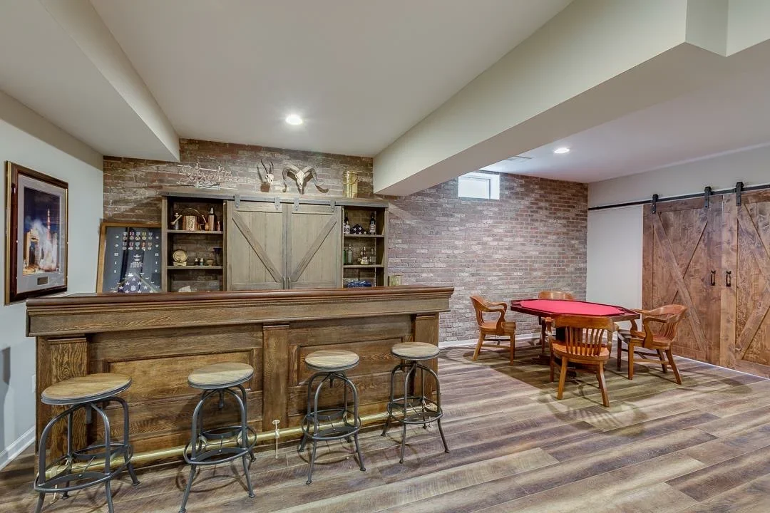 Finished basement with wood bar, brick wall, hardwood floors, and game room furniture