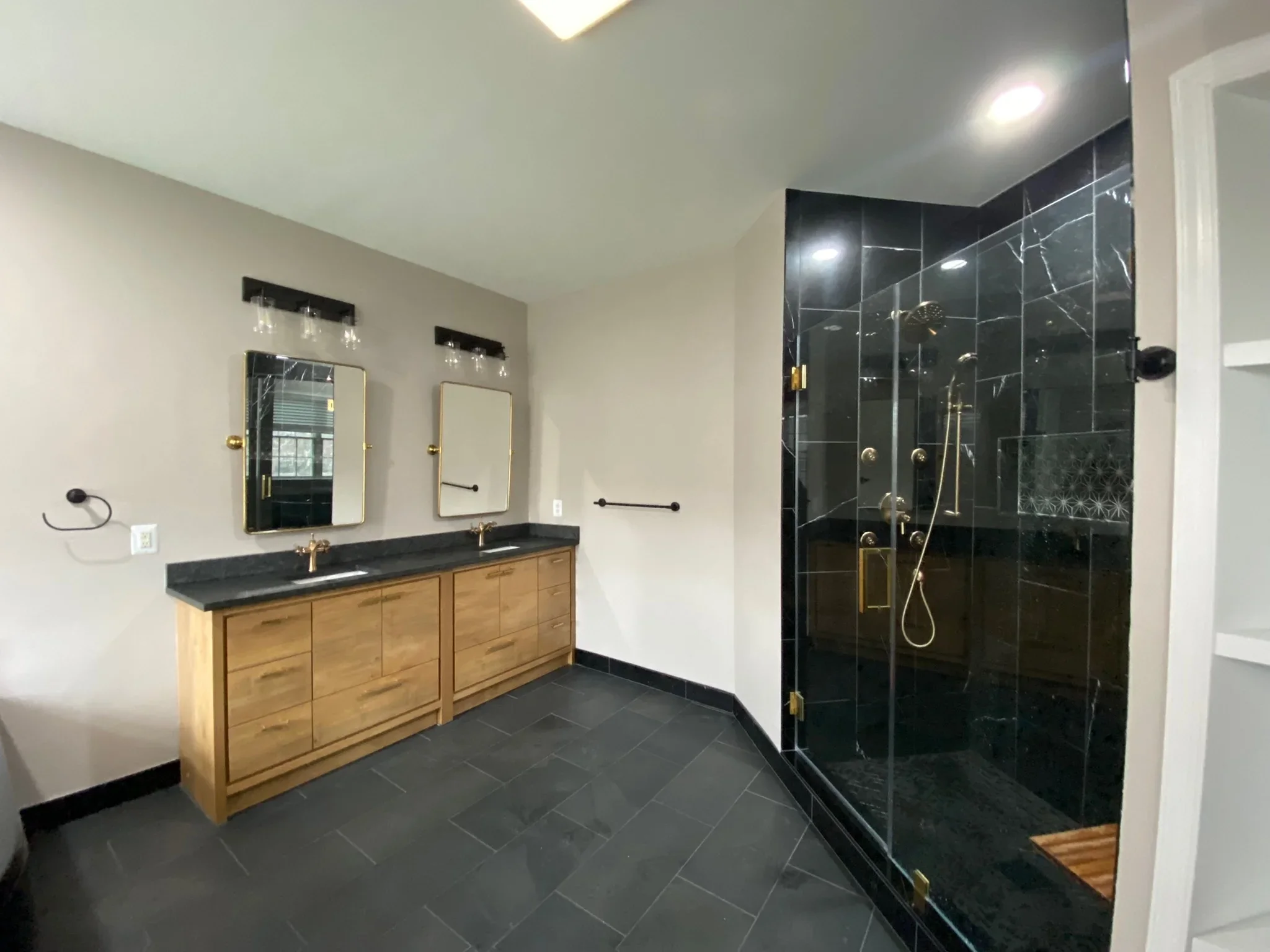 Master bathroom with wood vanity, black marble tile shower, and frameless glass enclosure