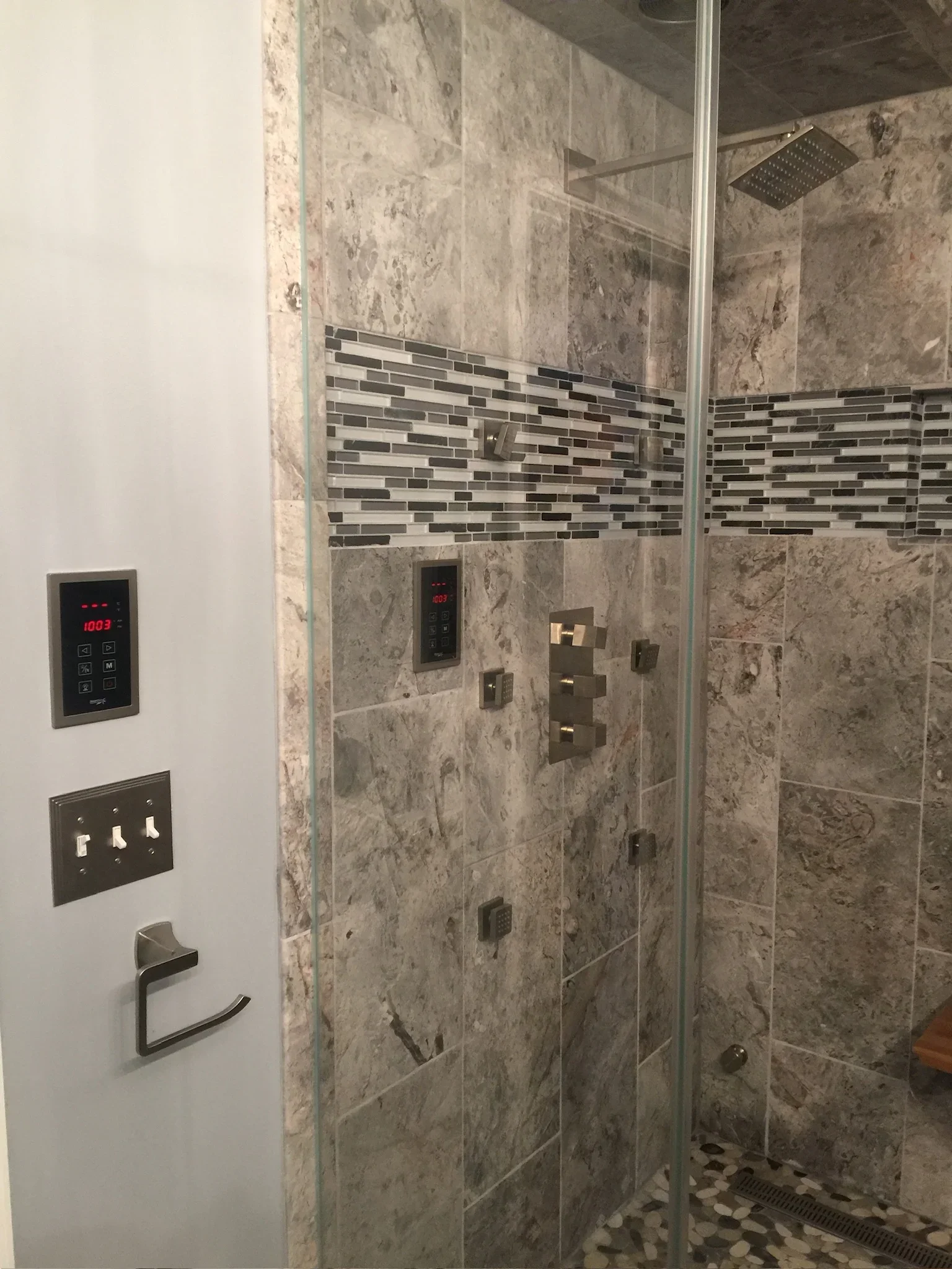 Travertine tile shower with mosaic accent band, frameless glass door, and digital controls