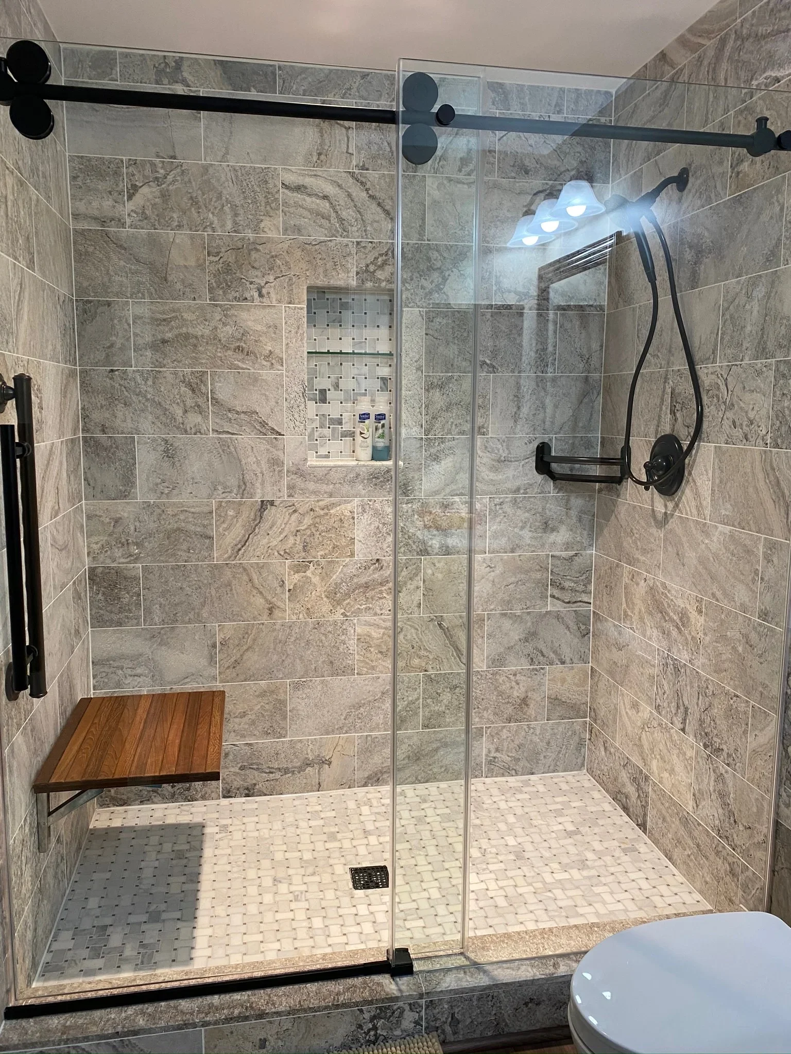 Walk-in shower with stone tile walls, frameless glass door, and matte black fixtures