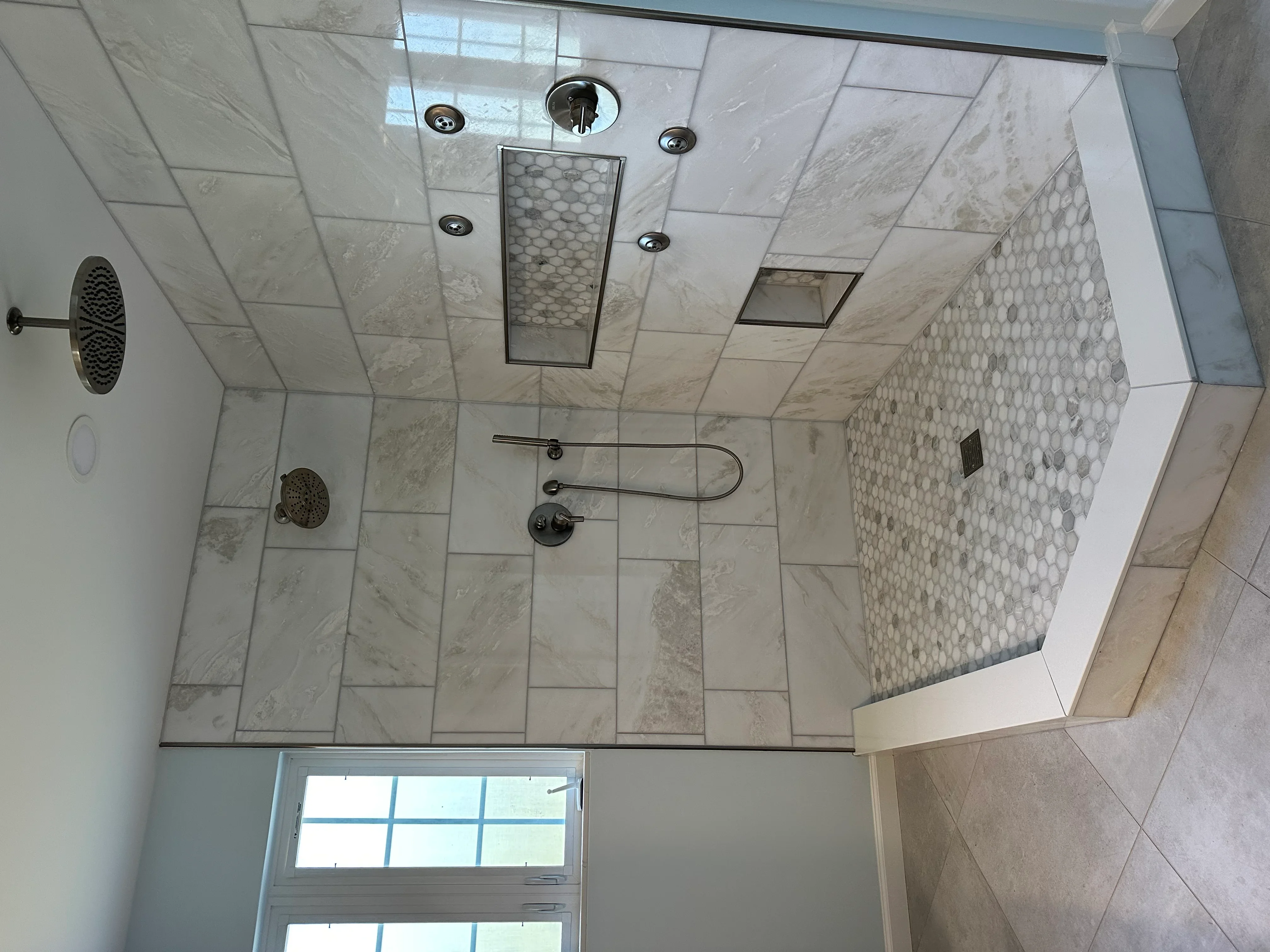 Marble tile shower with frameless glass door, dual showerheads, and penny-round accent tile