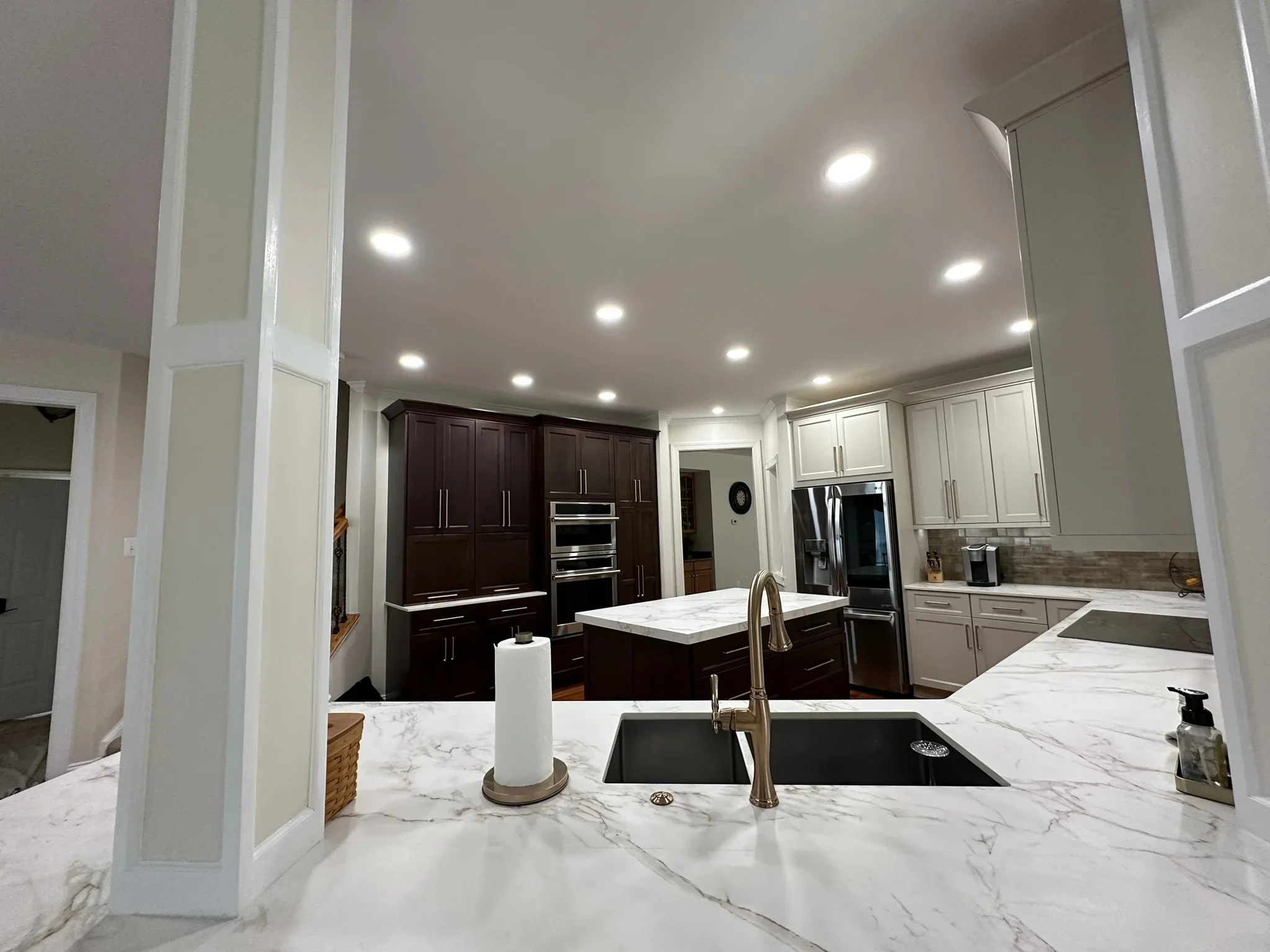 Modern kitchen with white marble counters, dark and white cabinetry, stainless steel appliances, and recessed lighting