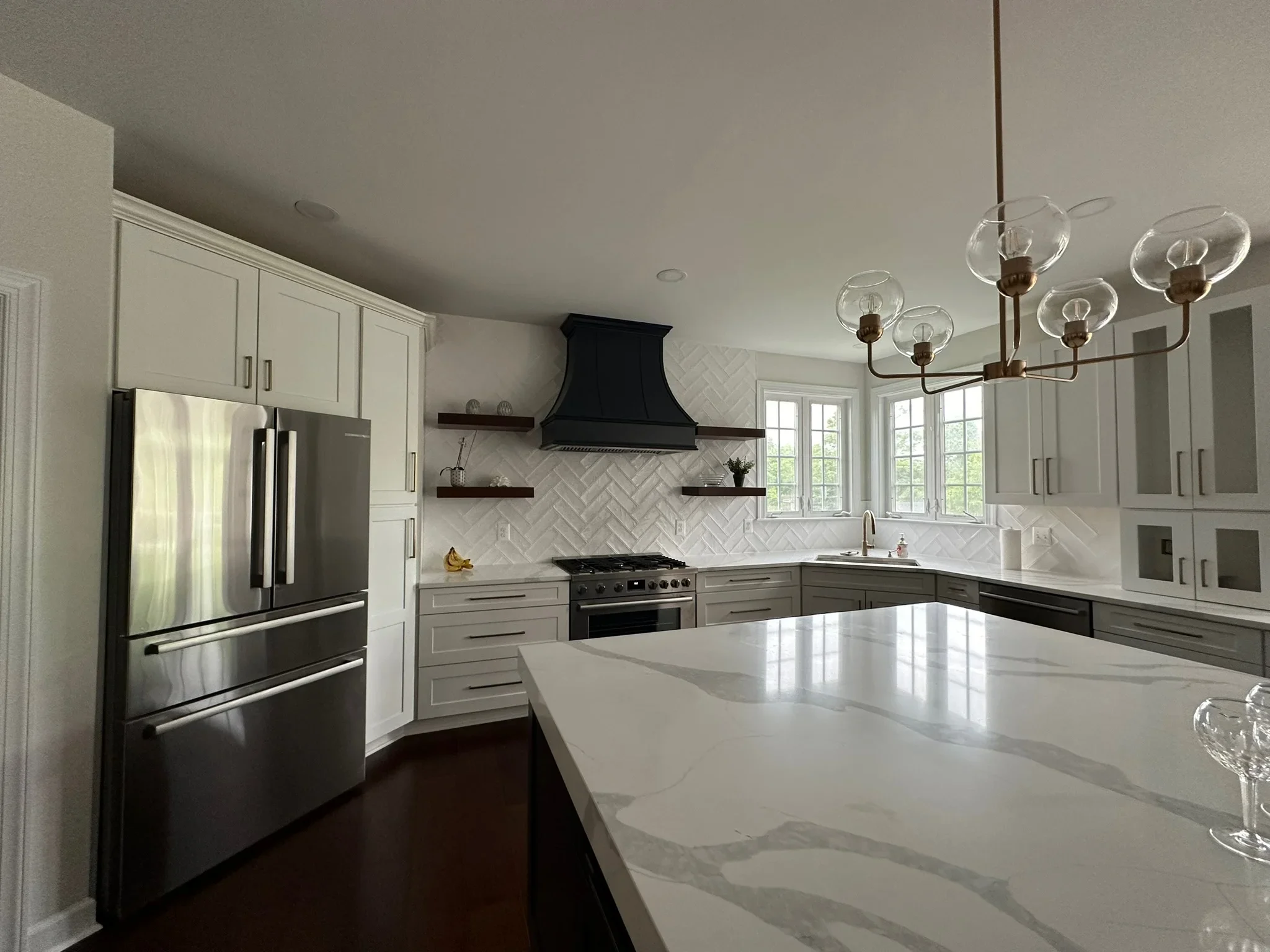 White kitchen with herringbone tile backsplash, black range hood, quartz island, and stainless steel appliances