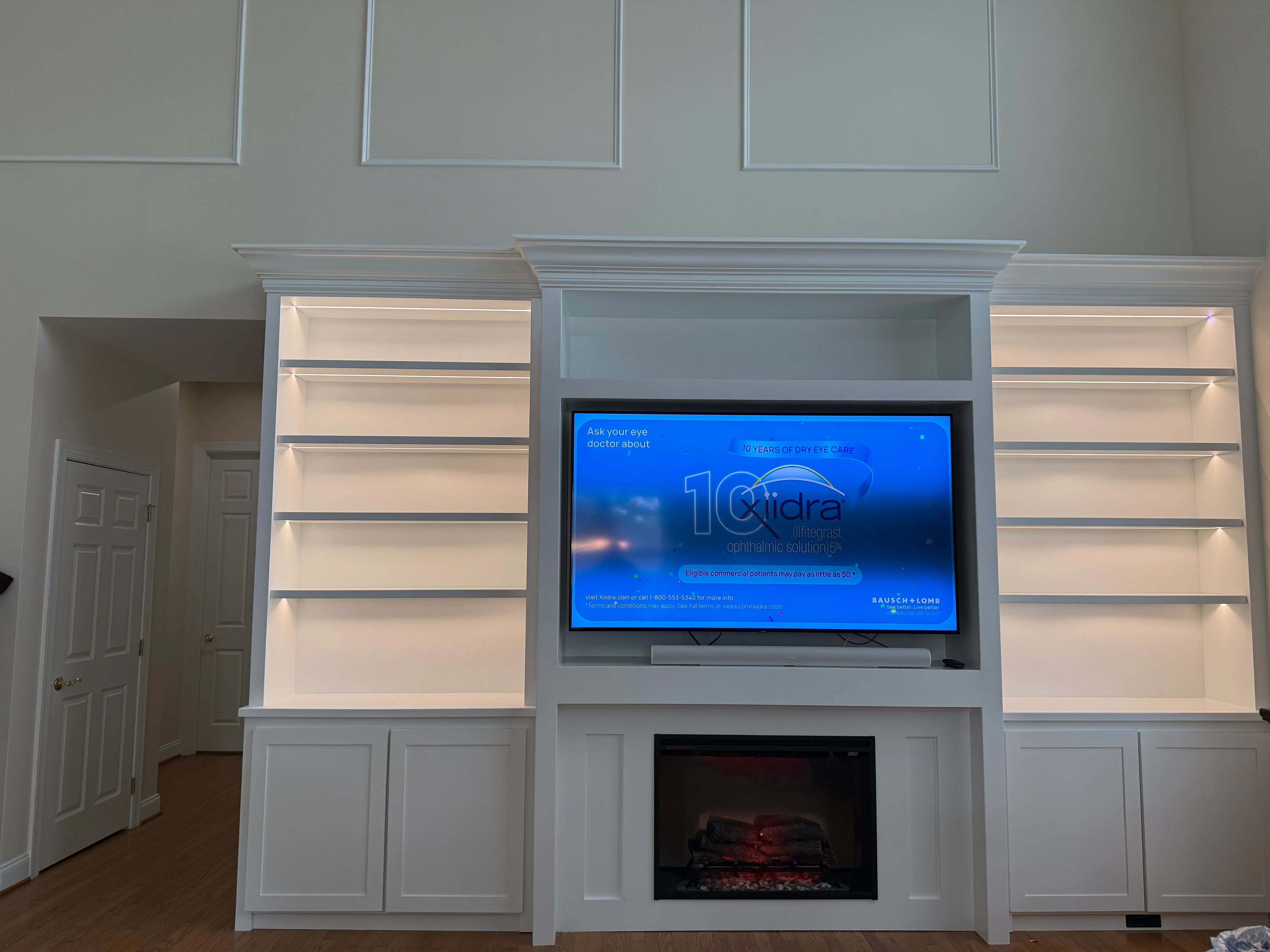 White built-in cabinetry with illuminated shelves, fireplace, and mounted TV display
