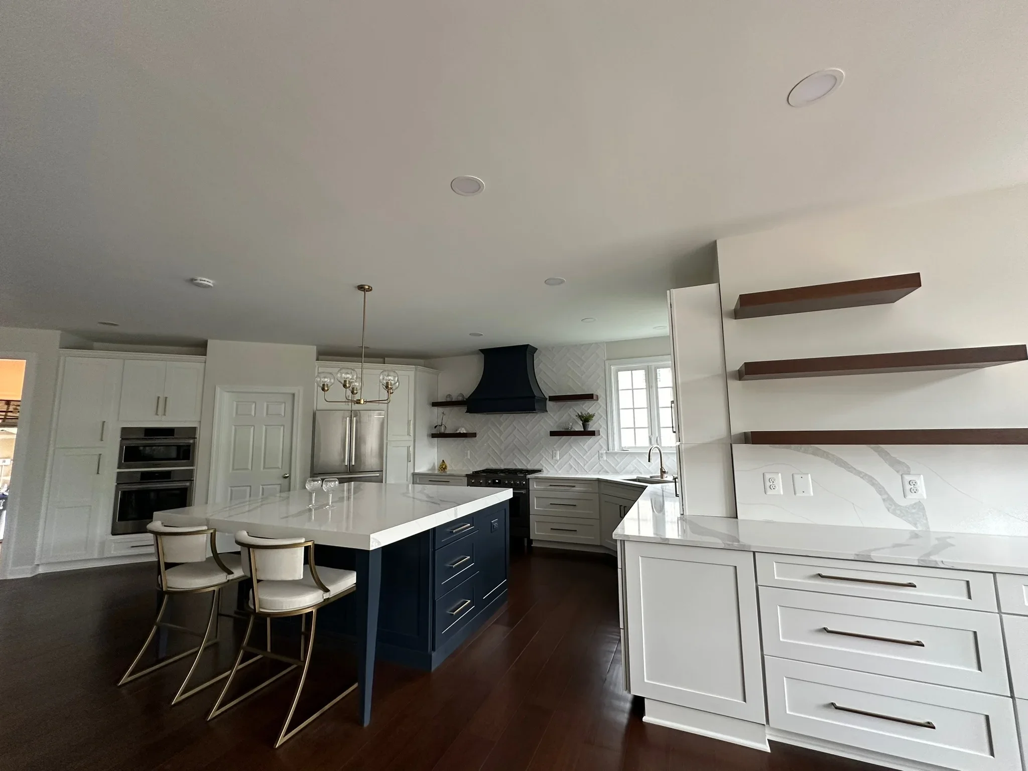Modern kitchen with white and navy cabinetry, quartz counters, herringbone backsplash, and wood shelving