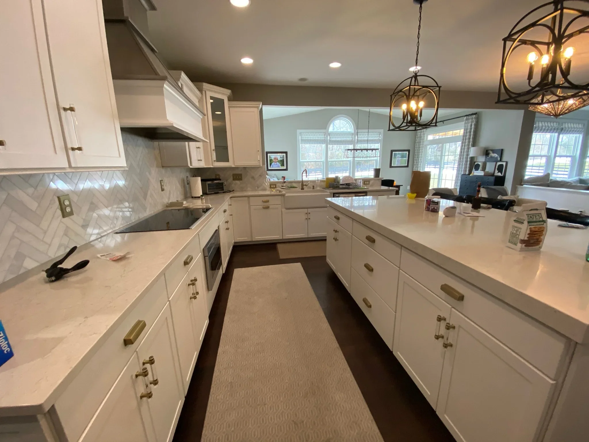 White kitchen with quartz counters, herringbone backsplash, white cabinetry, and pendant lighting
